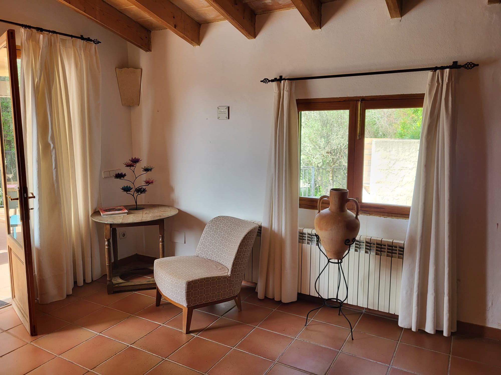 A quiet corner at Casa Romana with an armchair, round table and terracotta jug by the window